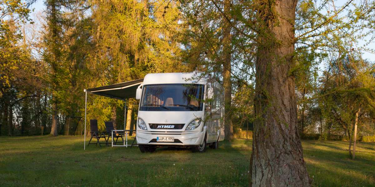 Campmobil in grüner Natur, mit Sitzgruppe unter der Markise